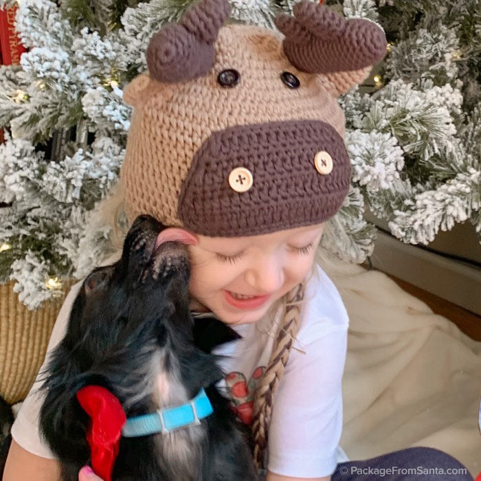 Little girl wearing a Reindeer Hat and her dog giving her kisses