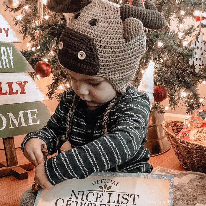 Package From Santa® - Young child looking at his Personalized Nice List Certificate and wearing a Reindeer Hat