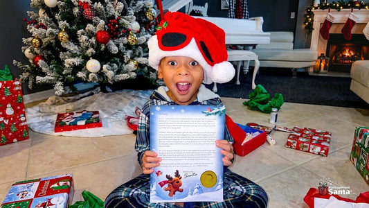 Boy in a Santa hat holding up his personalized letter from Santa beside the Christmas tree