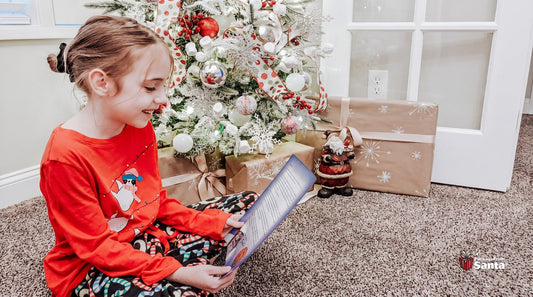 Girl in Christmas pajamas reading her personalized letter from Santa beside the tree