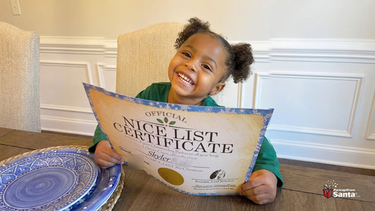A smiling girl holding up her Official Nice List Certificate from Santa at the kitchen table