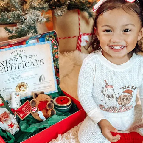 A smiling little girl beside her Nice List Certificate and opened Santa Letter Package